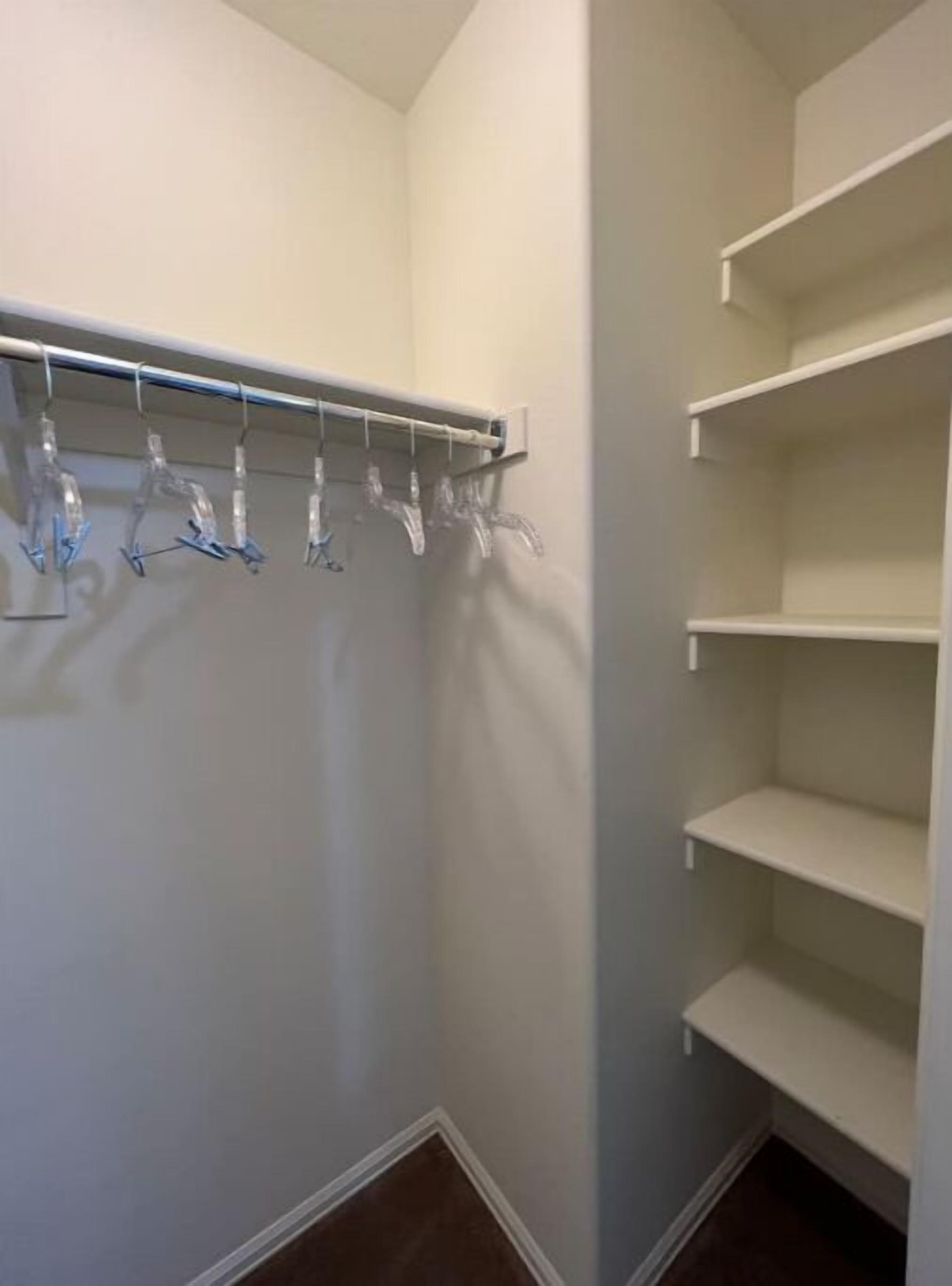 Un dressing avec une tringle métallique pour suspendre les vêtements et plusieurs étagères vides.