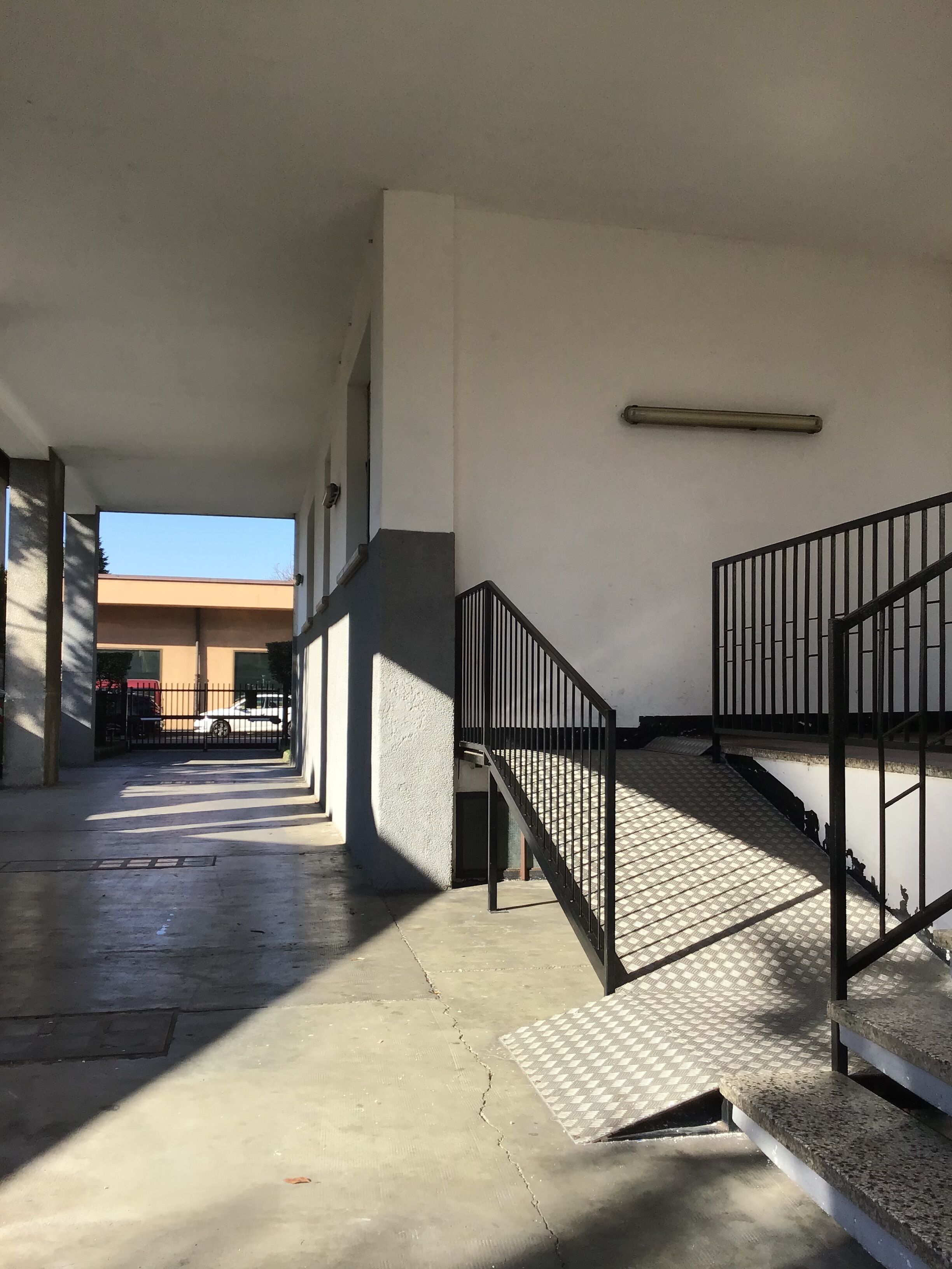 Ein überdachter Außenbereich mit Treppe, Betonboden und Metallgeländer.
