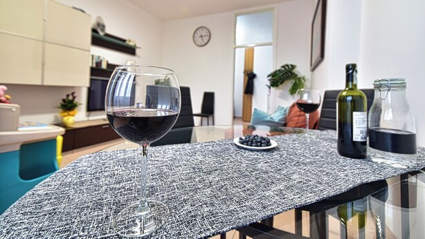 A dining table with a textured tablecloth, a glass of red wine, a bottle of wine, and a glass jar. - Whole cozy apartment ;Bright, ideal, for families;Single couples. (Lazzate)