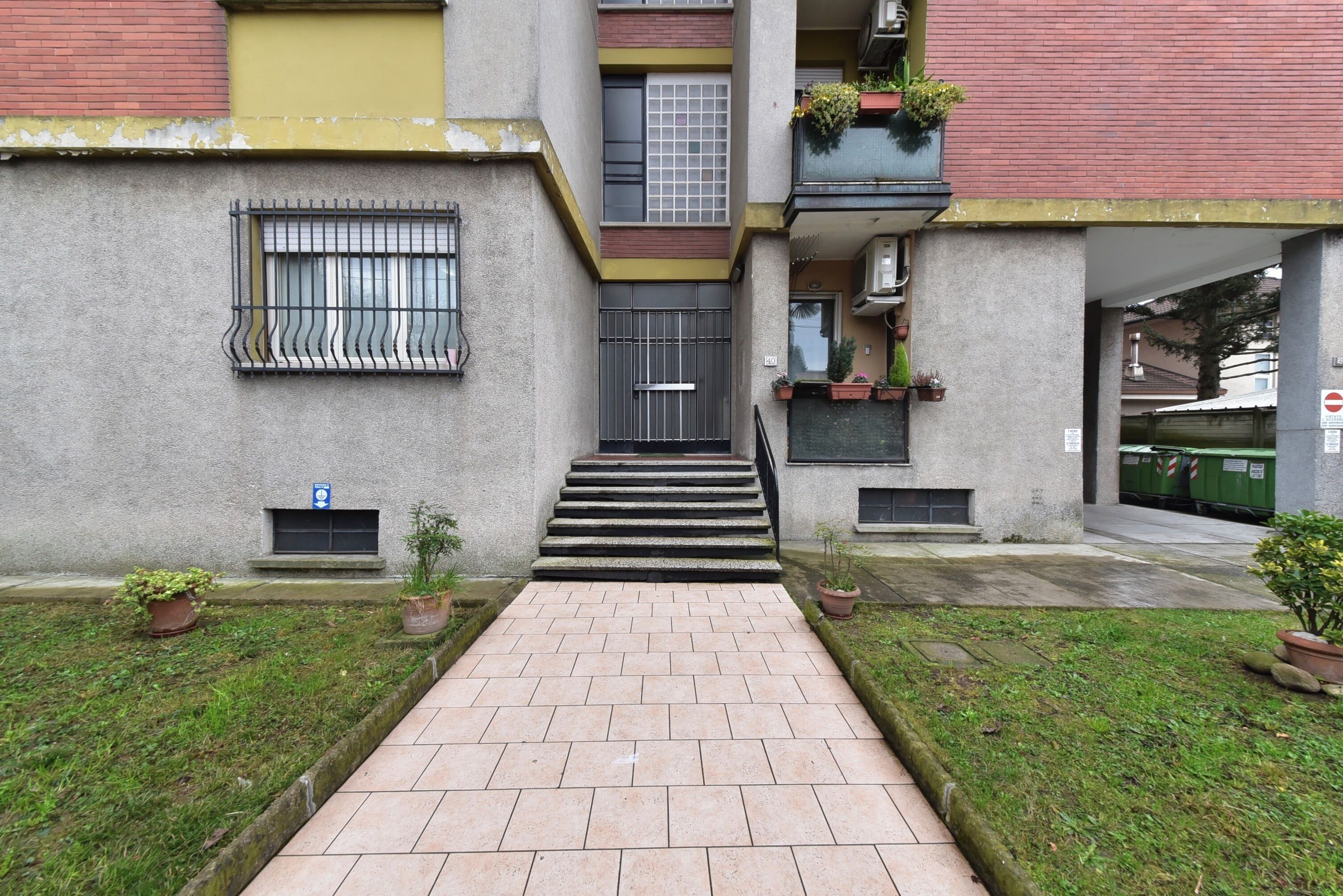 Un bâtiment doté d’un escalier central menant à l’entrée, de plantes en pot et d’une petite fenêtre avec un rideau.