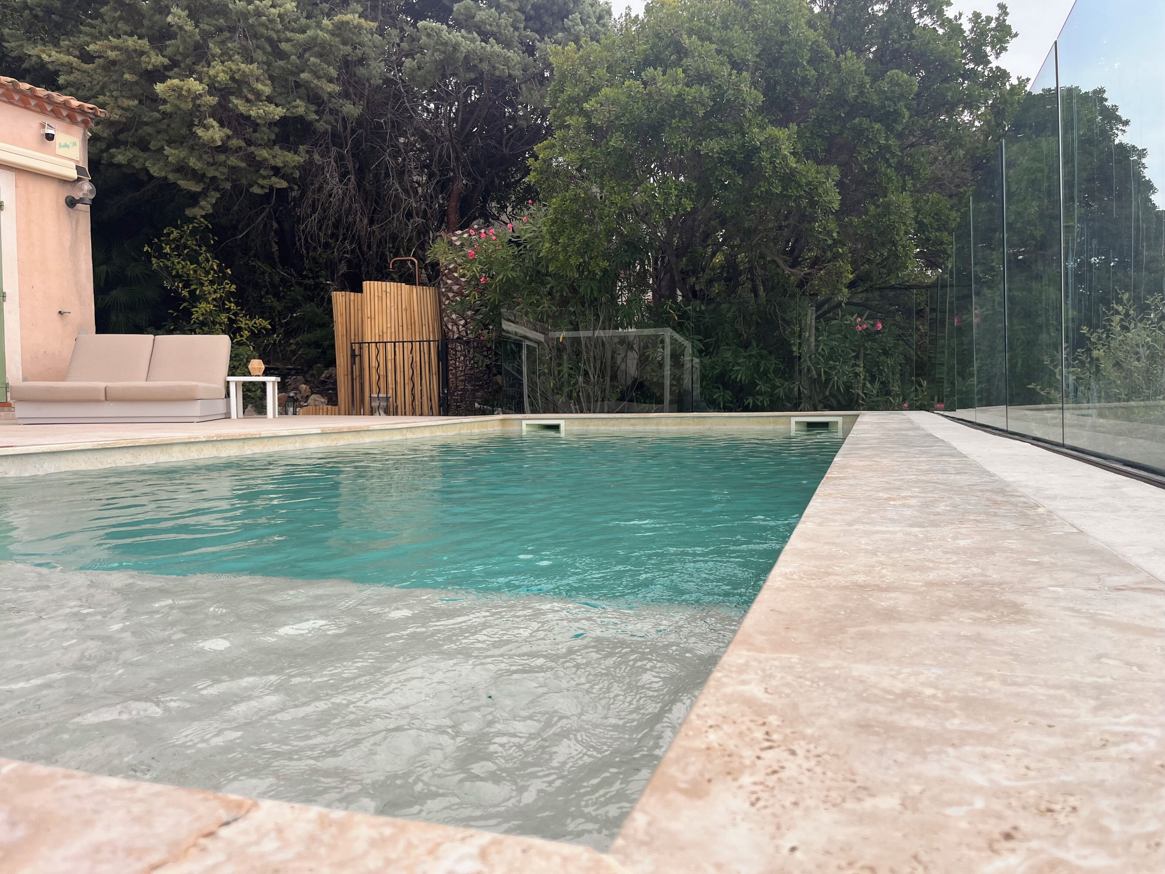A swimming pool with a tiled edge, surrounded by a fence, and a wooden structure in the background.