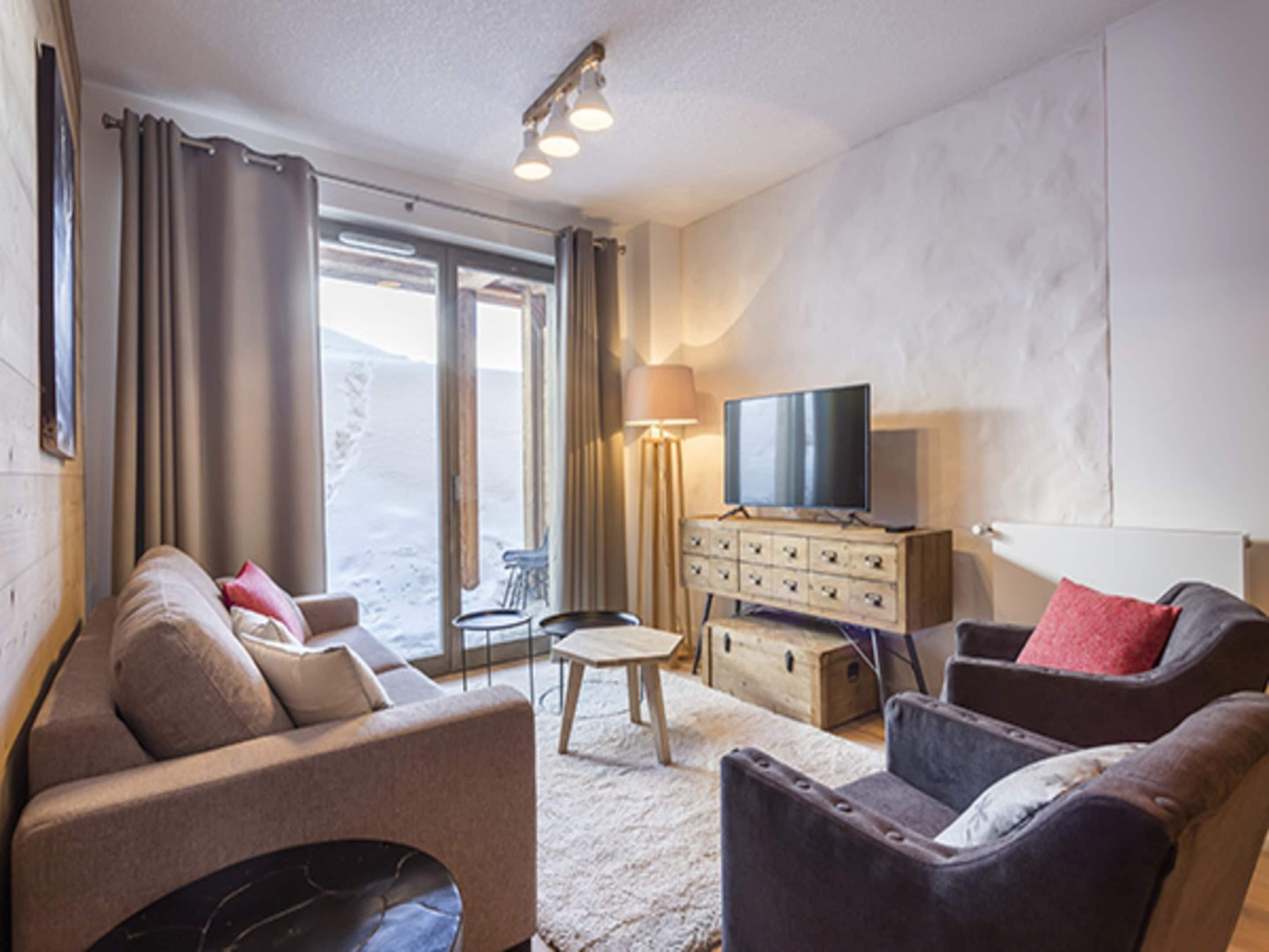 Una sala de estar con sofá, sillón, televisor, lámpara y vistas a través de un ventanal.
