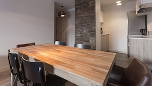 Un comedor moderno con una mesa de madera y sillas negras, una pared de acento de piedra y una cocina al fondo.