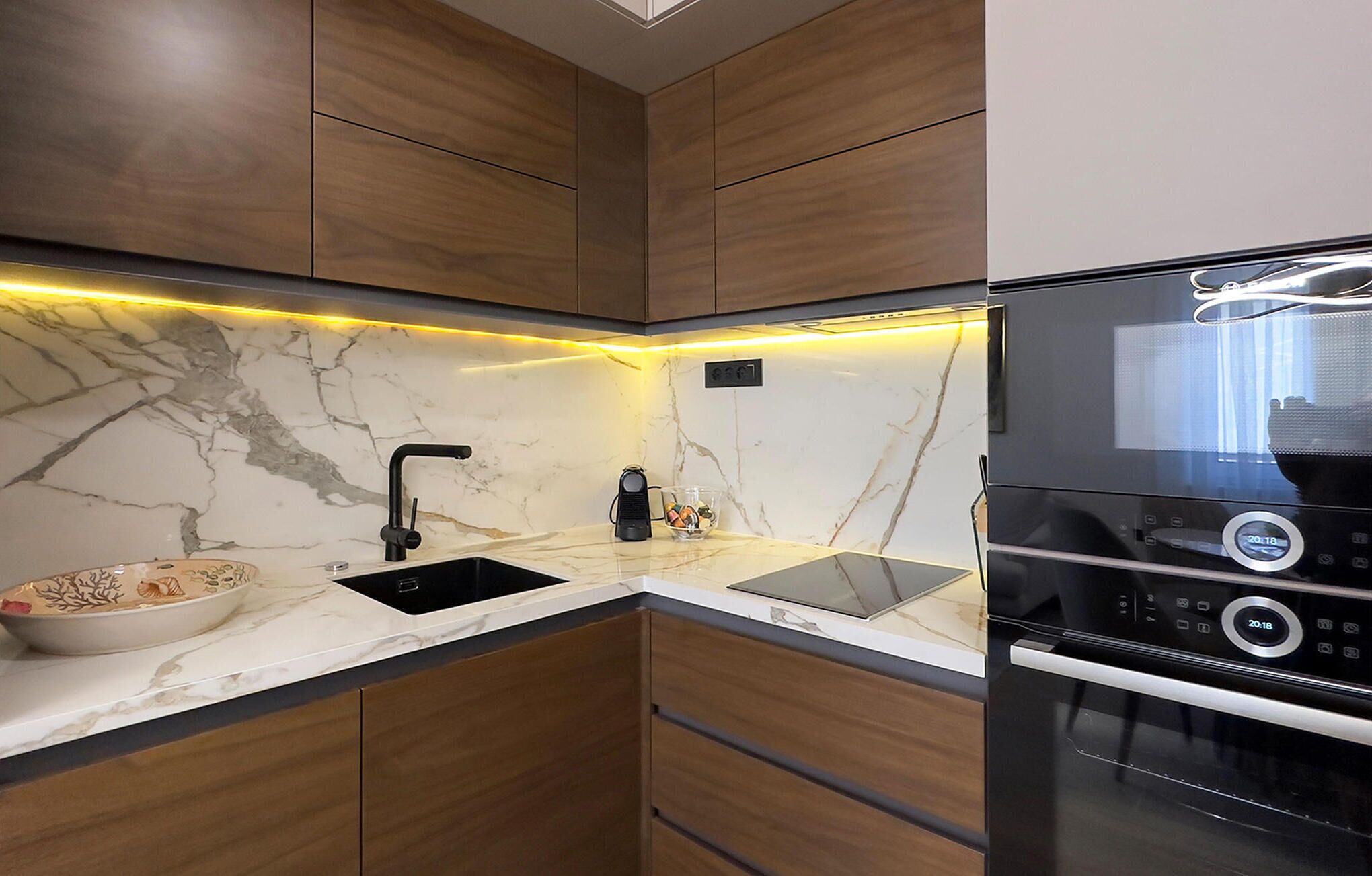 A modern kitchen with a built-in oven, a sink, and a marble countertop.