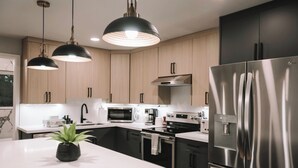 A modern kitchen with stainless steel appliances, wooden cabinets, and pendant lighting. - Rooftop Lake Union & Skyline Views -- New Eco Home in Wallingford (Seattle)