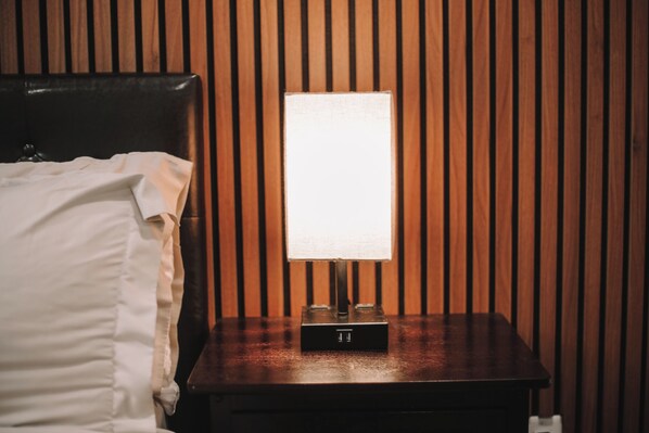 A wooden bedside table with a lamp, a bed with white bedding, and a wooden slat wall.