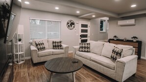 A living room with two sofas, a coffee table, a world map wall decoration, a window with blinds, and an air conditioning unit. - Rooftop Lake Union & Skyline Views -- New Eco Home in Wallingford (Seattle)