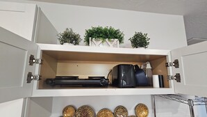 A white cabinet with a shelf containing a black coffee maker, a white kettle, and a small potted plant. Below the cabinet, there are decorative circular wall plates. - Mountain View Retreat Near Zion, Sand Hollow (Hurricane)