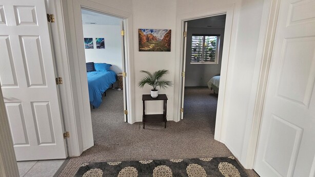 A hallway leading to a bedroom with a blue bedspread, a potted plant, and a painting on the wall. - Mountain View Retreat Near Zion, Sand Hollow (Hurricane)