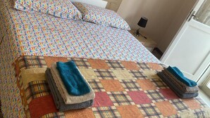 Un lit avec une couette aux motifs géométriques colorés et une couverture à carreaux. Deux serviettes pliées sont posées sur le lit.
