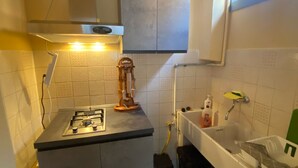 Une cuisine de taille réduite, équipée d’une cuisinière à gaz, d’un petit évier et d’une fenêtre située au-dessus de l’évier.