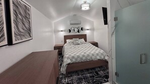 A bedroom with a bed, bedside tables, a desk, and a wall-mounted air conditioner.