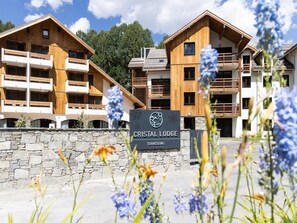 A sign for Cristal Lodge with a stone wall and wooden buildings in the background. - Apartment in Serre-chevalier Near Ski Slopes (Saint-Chaffrey)