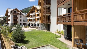 A multi-story hotel with wooden balconies, a well-maintained lawn, and a mountainous backdrop. - Apartment in Serre-chevalier Near Ski Slopes (Saint-Chaffrey)
