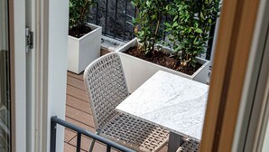 A balcony with a white table and wicker chairs, surrounded by potted plants and a grey wall. - Jacuzzi Suite – Nikis Collection Trastevere (Roma)
