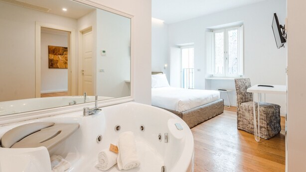 A modern bathroom with a large bathtub, a mirror, and a toilet. - Jacuzzi Suite – Nikis Collection Trastevere (Roma)