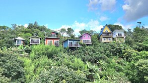 A row of colorful houses with balconies, surrounded by dense greenery. - Charming 1-bedroom chalet in lush Poas with cascading pools & raw nature  WiFi (Poas)