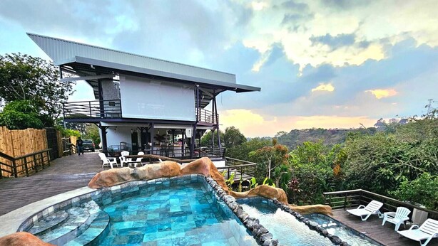 A modern pool area with a view of a mountain range, a wooden deck, and a building with a balcony. - Charming 1-bedroom chalet in lush Poas with cascading pools & raw nature  WiFi (Poas)