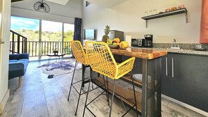 A modern kitchen with a dining area, featuring a large island, yellow chairs, and a TV. - Charming 1-bedroom chalet in lush Poas with cascading pools & raw nature  WiFi (Poas)