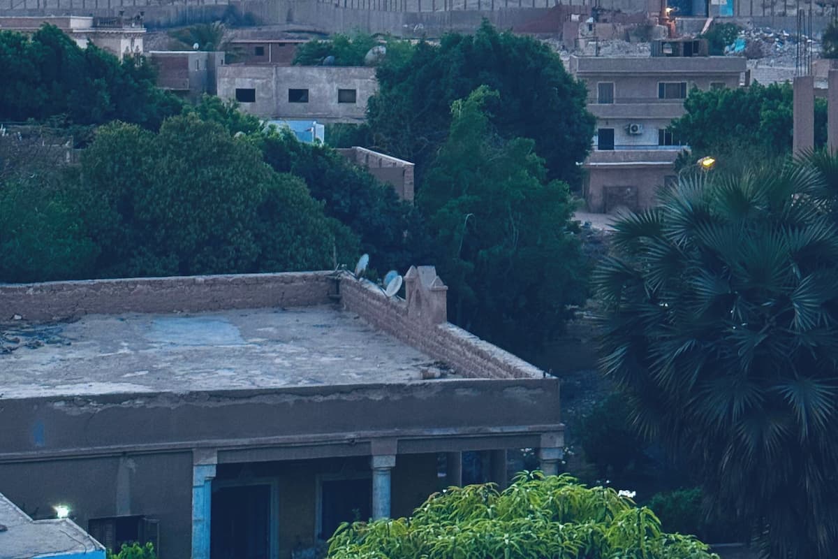 A pyramid with a flat top, surrounded by a fence, and a residential area with buildings and trees in the foreground.