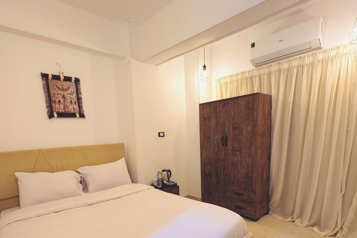 A bedroom with a large bed, a wooden wardrobe, a wall-mounted air conditioner, and a curtain.