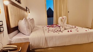 A hotel room with a bed, a nightstand, a telephone, and a view of a pyramid through the window. - Arena Pyramids View (Giza)