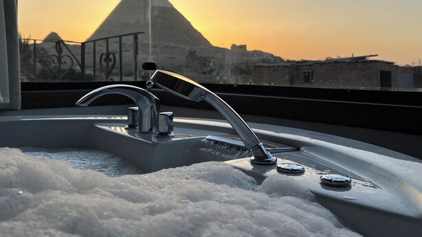A bathroom with a modern faucet and a view of a pyramid at sunset. - Arena Pyramids View (Giza)