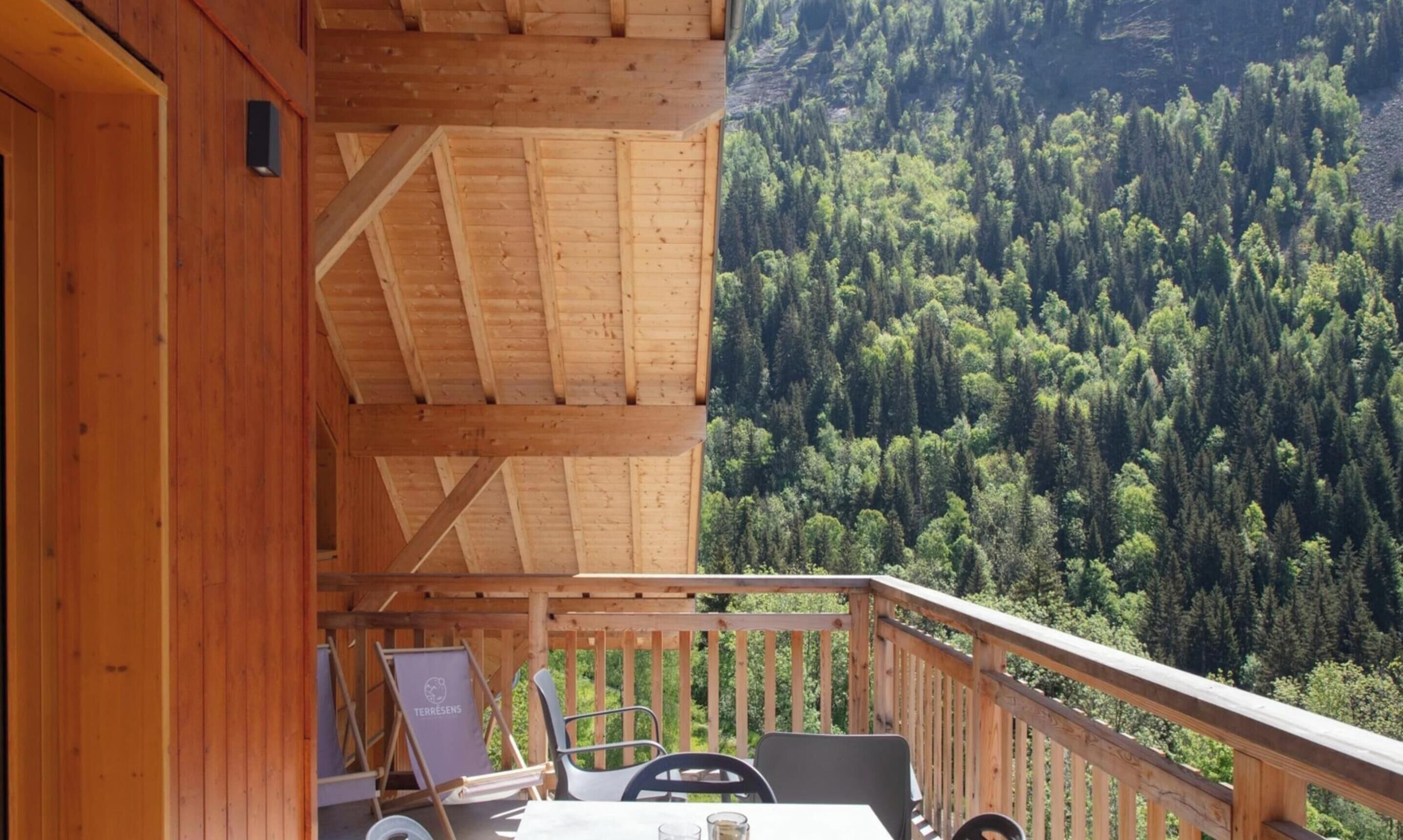 A wooden deck with a table and chairs overlooking a forested valley.