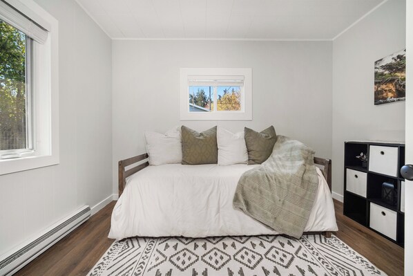 A bedroom with a bed, a window, a radiator, a patterned rug, and a black and white storage unit. - Cozy Olympic Haus, in Port Angeles near Olympic National Park, Lakes & Downtown (Port Angeles)