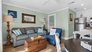 Ein Wohnzimmer mit grauem Sofa, blauem Sessel, einer Holzkiste und einem Esstisch.