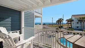 Ein Balkon mit weißen Geländern, der auf einen Pool und den Blick aufs Meer führt.