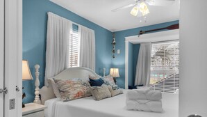 Ein Schlafzimmer mit einem Bett, Nachttischen, einem Deckenventilator und einem Fenster mit Jalousien.