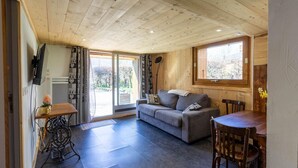 A cozy living room with a sofa, a dining table, and a TV mounted on the wall. - LE CHALET D'YVETTE - LA PLAGNE TARENTAISE (LA PLAGNE TARENTAISE)