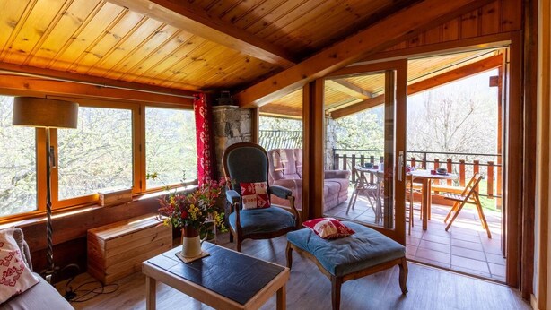 A cozy cabin interior with a wooden ceiling, a dining area with a table and chairs, a cushioned bench, and a large window offering a view of the outdoors. - LE CHALET D'YVETTE - LA PLAGNE TARENTAISE (LA PLAGNE TARENTAISE)
