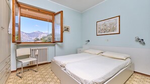 Una camera da letto con un letto, una sedia, un termosifone, una finestra con vista sulle montagne e un quadro appeso al muro.