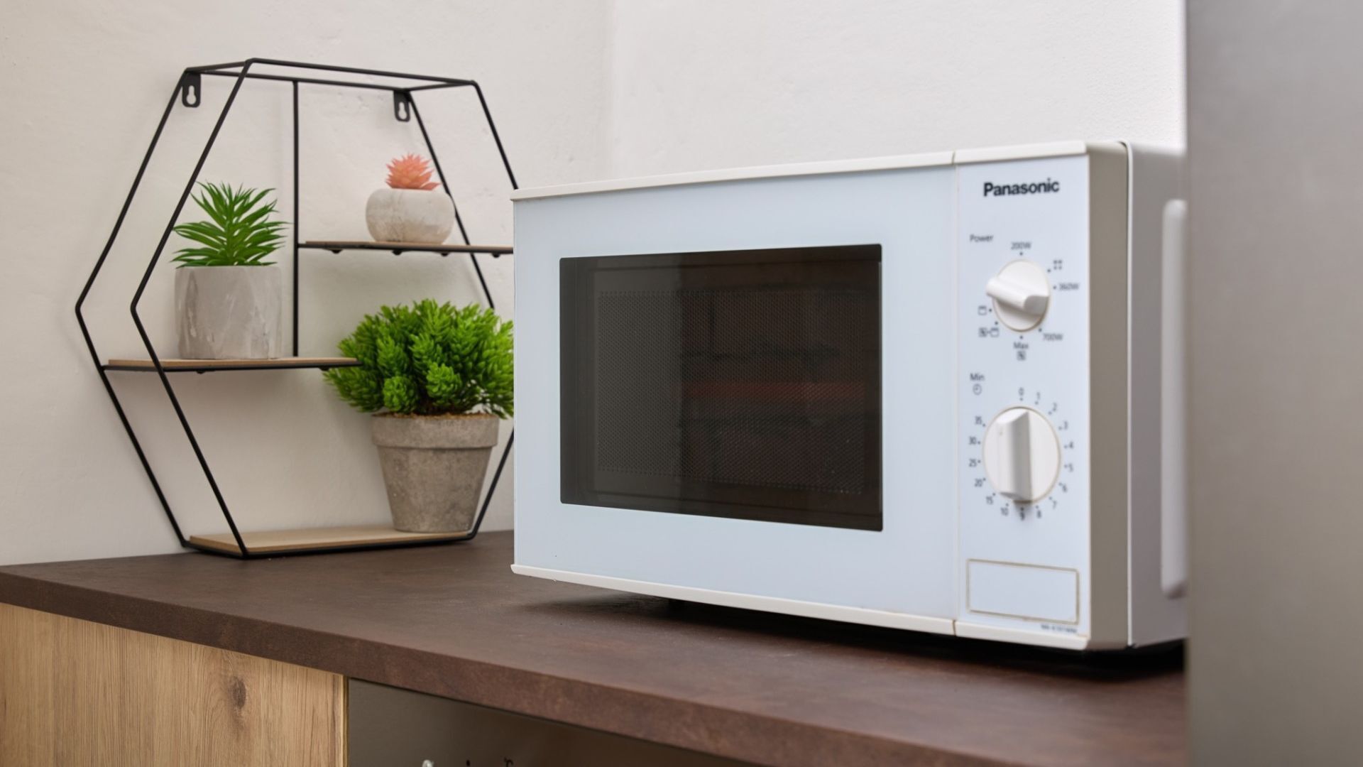 A Panasonic microwave on a kitchen counter with a hexagonal shelf holding plants.