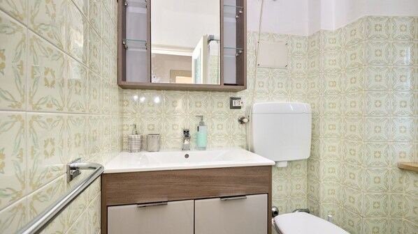 A bathroom with a white sink, a mirror, a toilet, and patterned tiles.