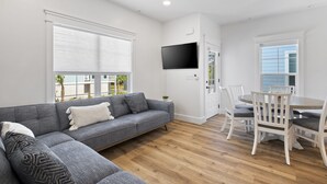 Una sala de estar moderna con un sofá gris, una mesa de comedor con sillas y un televisor de pantalla plana montado en la pared.