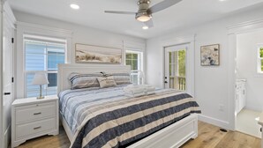 Un dormitorio con cama, mesitas de noche, ventilador de techo y ventana con persianas.