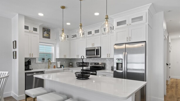 Una cocina moderna con armarios blancos, electrodomésticos de acero inoxidable y una isla central con taburetes de bar.
