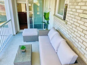 A balcony with a white sofa, a small table with a plant, and a glass door leading to an interior room. - Laval: Private Heated Pool • 3 Bedrooms • Piano (Laval)