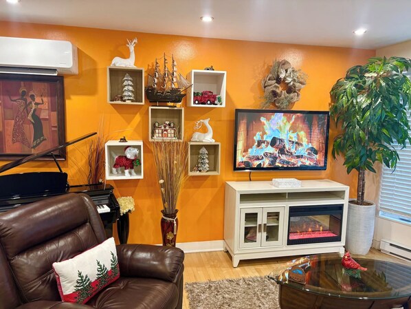 A living room with a fireplace, a television, a piano, and various holiday decorations. - Laval: Private Heated Pool • 3 Bedrooms • Piano (Laval)