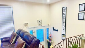 A reception area with a leather sofa, a staircase, a welcome sign, and a potted plant. - Spacious Zen Floor in Laval - Private Heated & Salt Pool, Garden & Piano (Laval)