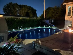 A swimming pool with a tiled deck, surrounded by a hedge and a wooden structure. - Laval: Private Heated Pool • 3 Bedrooms • Piano (Laval)
