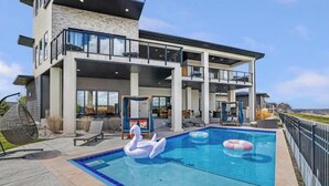A modern two-story house with a large swimming pool, outdoor seating, and a swan float.