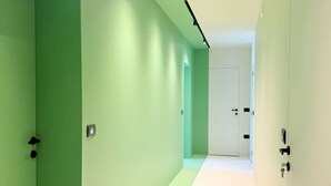 Um corredor com paredes verdes e chão branco, que leva a uma porta no final.