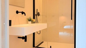 Um banheiro moderno com pia branca, acessórios pretos e box de vidro.