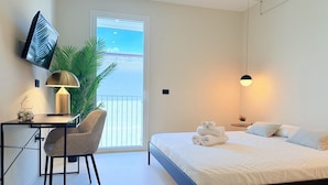 Una habitación de hotel moderna con cama, un escritorio con silla, televisor montado en la pared y un gran ventanal con vistas al exterior.