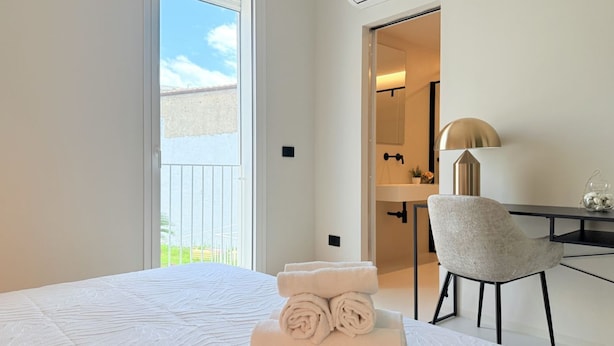 Habitación de hotel con cama, escritorio, silla y baño visible a través de una puerta abierta.