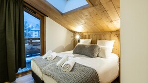 Un dormitorio acogedor con un tragaluz, una cama con toallas enrolladas y vistas a un paisaje nevado.